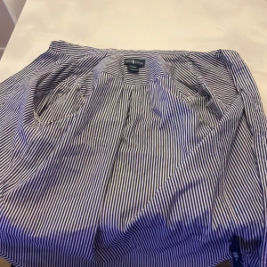 Blårandig skjorta från Ralph Lauren - Klassisk blårandig skjorta från Ralph Lauren med vit knappstängning och broderad logga på bröstet. Skjortan har lång ärm och är tillverkad i ett mjukt bomullsmaterial.  Den har en liten fläck på sig som man inte tänker på. Men går säkert bort i tvätten. OBS! Den är i storlek L i ungdoms storlek. 