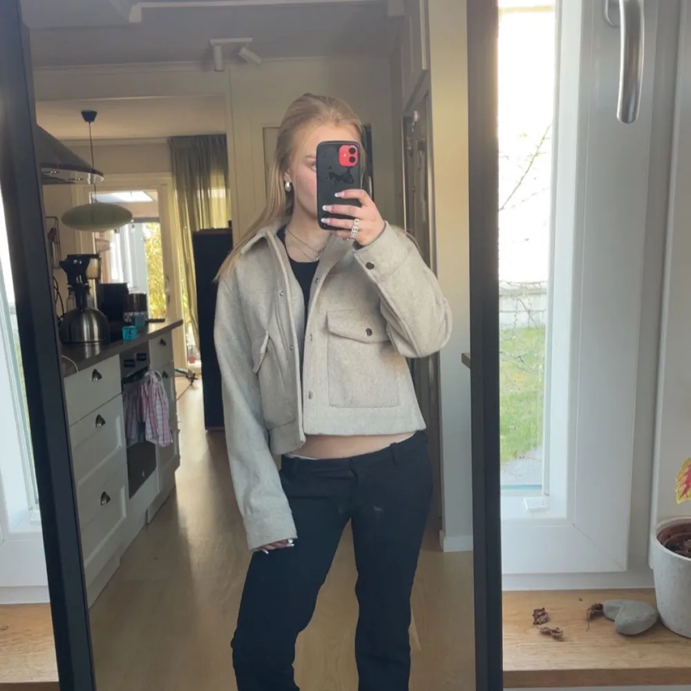 Säljer en beige croppad jacka med stora fickor framtill och knappar. Jackan har lång ärm och en stilren, enkel design som passar perfekt till vardags. Materialet känns mjukt och jackan har en modern passform.. Takit.
