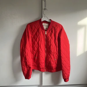Röd vårjacka - Röd kortare jacka med gulddetaljer. Dragkedja och två fickor med knapp.