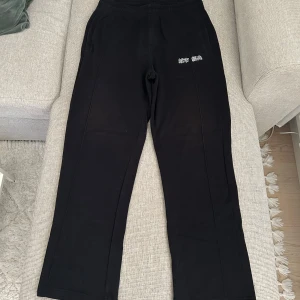 Svarta mjukisbyxor med broderad text - Säljer ett par svarta mjukisbyxor med broderad vit text på ena sidan från Urban Classic. Byxorna har normal passform och raka ben, samt resår i midjan för extra komfort. Perfekta för en avslappnad stil.