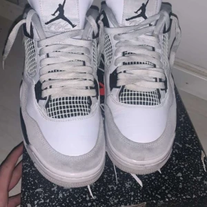 Nike Air Jordan 4 Retro White/Black äkta - Säljer ett par Nike Air Jordan 4 Retro i vitt, svart och grått. Skorna har klassisk meshpanel på sidorna, svarta detaljer och Jumpman-logga på plös och häl. Perfekta för dig som gillar streetwear och sneakers med ikonisk design. Kommer även med kvitto från coolkicks från en Americans butik