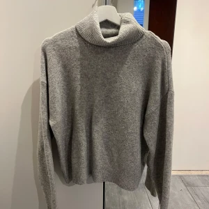 Grå polotröja från H&M - Mysig grå polotröja från H&M i mjukt stickat material. Tröjan har lång ärm, hög polokrage. .