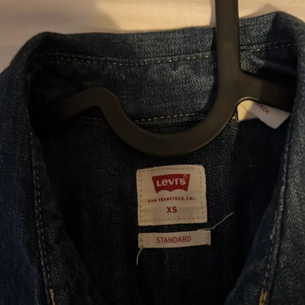 Mörkblå jeansskjorta från Levi's med klassisk westernstil. Skjortan har långa ärmar, tryckknappar och två bröstfickor med lock. Snygga kontrastsömmar och ikonisk röd Levi's-tagg på fickan. Perfekt för en avslappnad look.. Paidat.