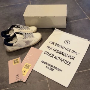 Golden goose - Snygga vita sneakers från Golden Goose med grå stjärndetalj på sidan och mörkblå häl. Helt nytt skick, säljes pga av att dom var för små. Bara att höra av sig vid funderingar🙌