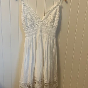 Vit klänning från Zara - Säljer en super fin vit klänning från Zara med spetsdetaljer. Klänningen har en v-ringad design och är ärmlös, perfekt för sommaren eller skolavslutning. I ett lätt och luftigt material.❤️