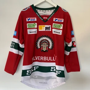 Fröulunda hemmatröja  - Säljer en röd Frölunda Indians hockeytröja från säsongen Storlek 140 i hyfsat skick finns tecken på använd längst ned på ryggen annars bra skick. 
