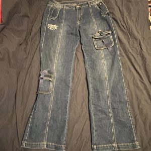 Jeansbyxor från Ed Hardy - Snygga jeansbyxor från Ed Hardy med broderad logga på framsidan och baksidan. Byxorna har flera fickor med lock och spännen🫶🏻