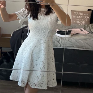 Studentklänning  - Elegant vit spetsklänning med korta ärmar och vackra blommiga detaljer. Klänningen har en dragkedja i ryggen och en fin passform. Nypris är 999kr.