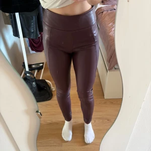 Vinröda leggings i läderimitation  - Snygga vinröda leggings i läderimitation med hög midja. De är fodrade på insidan så de är perfekta till vår, vinter och höst. En skada vid dragkedjan på sidan. 