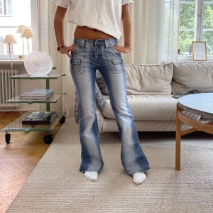 Blå bootcut jeans - MIDJEMÅTT: 37cm INNERBENSLÄNGD: 78 cm. Snygga blå bootcut jeans med en lätt tvättad look och flera fickor fram och bak. Perfekta för en avslappnad stil med en touch av retro. De har en lågmidjad passform som ger en cool och bekväm känsla.