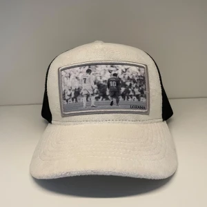 Vit och svart keps från Lozama med fotbollsmotiv - Snygg Velvet keps från Lozama i vit och svart med ett coolt fotomotiv på framsidan. Kepsen har en svart mesh-baksida för bra ventilation och justerbar passform. Perfekt för en avslappnad stil. Helt oanvänd! Bara att höra av sig vid frågor! Har även en annan Velvet keps utlagd om man vill köpa båda till ett mycket bra pris!