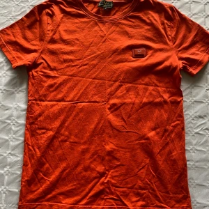 Orange t-shirt från 19V69 Italia - Säljer en snygg orange t-shirt från 19V69 Italia. T-shirten har en klassisk passform, korta ärmar och en patch med logga på bröstet. Perfekt för dig som vill sticka ut med färg i vardagen!