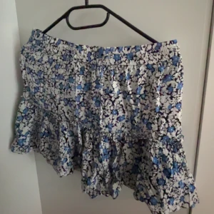 Blommig kortkjol med shorts under från Zara - Supersöt kortkjol med shorts under. Använd 2-3 gånger. Stolek m men passar bara till s och xs. Blått och svart blommönster på vit botten. Kjolen har volang och knyt i midjan för extra detalj. Perfekt till sommar.
