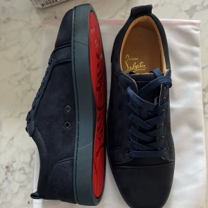 Mörkblå sneakers från Christian Louboutin - (Pris kan diskuteras) Säljer ett par mörkblå sneakers från Christian Louboutin med klassisk röd sula. Skorna har rund tå, snörning och är tillverkade i mocka med detaljer i skinn. Perfekta för dig som vill ha en stilren och lyxig look.