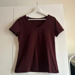 Vinröd t-shirt med v-ringning - En enkel och stilren vinröd t-shirt med v-ringad hals. T-shirten har korta ärmar och är tillverkad i ett mjukt material som passar perfekt till vardags. Snygg att matcha med jeans eller kjol.