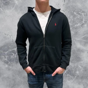 Ralph Lauren Full Zip Hoodie Svart - •Ralph Lauren Full-Zip Hoodie Svart. Skick: 8/10, Inga skador! Storlek: 14/16 år = XS~. Modell: 173 cm, 65 kg. Sitter något litet på modellen på bild! Authentic: ✅, QR Kod finns även i plagget! Hör av dig vid frågor eller funderingar, mvh Hessler’s;)