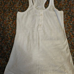 Vit linnetopp från Dr. Denim - Säljer en stilren vit linnetopp från Dr. Denim. Toppen har knappar framtill och är ärmlös med en racerback-design. 