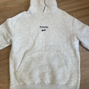 Grå hoodie från Pull&Bear - Säljer en stilren grå hoodie från Pull&Bear med tryck på både fram- och baksidan. Hoodien har en klassisk känguruficka och ribbade muddar. Perfekt för en avslappnad stil.