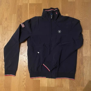 Sail Racing windbreaker - Super schysst vindjacka som värmer, perfekt till hösten i väldigt bra skick. Storlek small men sitter som en medium. Inga skador i yttertyget eller i fodret. Nypris runt 2000. Hör av er om frågor!