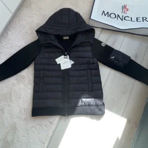  Moncler jacka - Snygg svart dunjacka från Moncler med huva och dragkedja. Jackan har långa ärmar och en quiltad design på framsidan. Perfekt för kyligare dagar med stil.