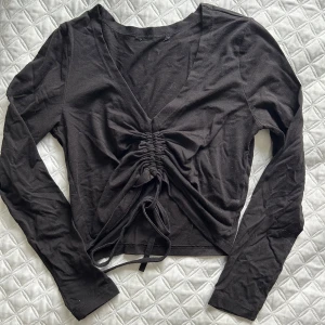 Svart långärmad topp med knyt - Snygg svart långärmad topp med v-ringning och knytning framtill. Perfekt för en stilren look. Har själv använt tröjan bak och fram så att knytningen blir i ryggen, jättesnyggt😍