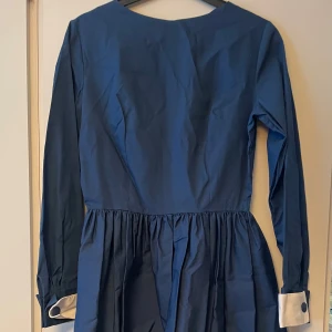 Blå Retroklänning med fina detaljer i stl XS/S - Blå klänning i sailorstil med tillhörande bälte, stl XS/S, uppskattas passa stl 34/36, midja 67 cm, byst 35 cm. Min mammas klänning som hon fick uppsydd som ung, 50/60 tal, och sen aldrig använde, har bara hängt i en garderob så är i oanvänt & felfritt skick, en ångning sen är du good to go! :) 