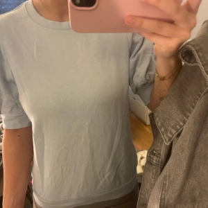 Ljusblå topp med puffärmar - Säljer en söt ljusblå topp med puffärmar. Toppen har en rund halsringning och korta ärmar som ger en fin detalj. Perfekt för en avslappnad stil.