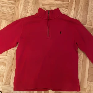 Röd halvzip tröja från Polo Ralph Lauren - Säljer en röd långärmad tröja från Polo Ralph Lauren med halv dragkedja och klassisk broderad logga på bröstet. Perfekt för en stilren och avslappnad look. Hög krage och mjukt material. Den är använd men är som ny. Utmärkt skick. Pris kan diskuteras