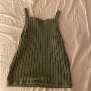 Grön ribbad linnetopp från H&M - Säljer en stilren grön ribbad linnetopp från H&M. Perfekt för varma dagar med sin ärmlösa design och bekväma passform. Passar utmärkt till både jeans och kjol.