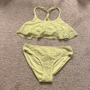Grön spetsbikini från Lindex - Snygg gul bikini från Lindex med spetsdetaljer. Överdelen har en volang och smala axelband som korsas i ryggen. Perfekt för soliga dagar på stranden!