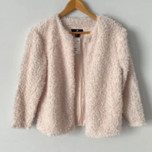 Beige teddyjacka från H&M - Mysig beige teddyjacka från H&M som är perfekt för kyliga dagar. Jackan har en fluffig textur och är långärmad, vilket gör den både stilren och bekväm. Perfekt för att hålla värmen med stil!