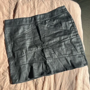 Svart kjol med dragkedja - Snygg svart kortkjol med dragkedja bak. Kjolen har en stilren design med diagonala sömmar som ger en cool look. Perfekt för att matcha med olika toppar och accessoarer.