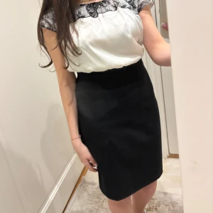 Svart och vit klänning med spetsdetalj - Säljer en elegant svart och vit klänning med smal passform. Överdelen är vit med svart spets vid halsringningen och axlarna, medan kjolen är helsvart och rak. Perfekt för dig som gillar stilrena kontraster och feminina detaljer.