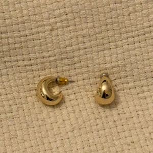 Guldiga droppformade örhängen - Säljer ett par stilrena, droppformade örhängen i guldig färg. Perfekta för dig som gillar minimalistiska accessoarer med en modern touch. Passar till många olika stilar och tillfällen.