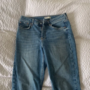 Blå jeans med råa benslut från Gina Tricot - Säljer ett par klassiska blå jeans från Gina Tricot med raka ben och råa, fransiga benslut. Jeansen har normal passform, fickor och stängs med dragkedja och knapp. Perfekta till vardags för en avslappnad look.