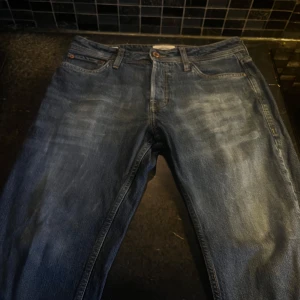 Blå jeans från jack & Jones  - Snygga blå jeans från Jack & Jones med klassisk femficksdesign och knappgylf. Perfekta för en avslappnad stil. Märkeslappen i läder baktill ger en autentisk touch.