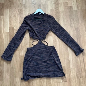 Mörk kortklänning från Divided H&M - Snygg kortklänning från Divided H&M i mörka toner av brun, blå och grå. Klänningen har lång ärm, coolt randigt mönster och trendiga cut-outs med snörning i midjan. Materialet är mjukt och stretchigt, perfekt för dig som vill sticka ut.