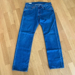 Levi's 501 - Klassiska Levi's 501 jeans i blå denim med raka ben och normal passform. Byxorna har fem fickor, knappgylf och den ikoniska läderpatchen bak i midjan. Perfekta för dig som gillar tidlös stil och vill ha ett par riktigt schyssta jeans.