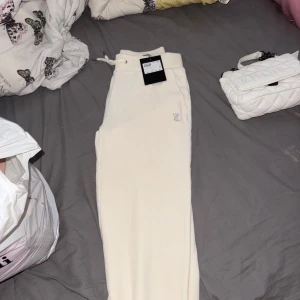 Juicy Couture vita mjukisbyxor - Krämvita mjukisbyxor från Juicy Couture med glittrande 'Juicy' i strass över baken. Byxorna har dragsko i midjan och är gjorda i mjuk bomullsmix. Perfekta för en chill och trendig look. Med tillhörande Hoodie. Helt nytt.