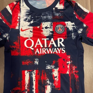 PSG x Nike Dri-Fit fotbollströja S - Paris Saint-Germain fotbollströja från Nike i slim fit-modell. Tröjan har ett unikt abstrakt mönster i rött, marinblått och vitt med klubbmärke och Qatar Airways-tryck på bröstet. Tillverkad i lätt Dri-Fit-material som andas. Perfekt för dig som älskar PSG och vill sticka ut på planen. 