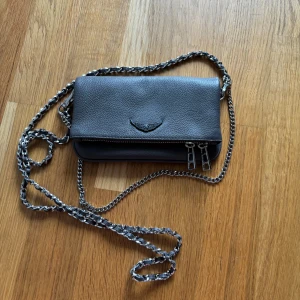 Grå axelväska från Zadig & Voltaire - Använd men i utmärkt skick, säljer då den inte kommer till någon användning längre. Dustbag ingår.  Höjd: 11cm Längd: 18.5cm Vidd: 2.5cm Handtag: 60cm 