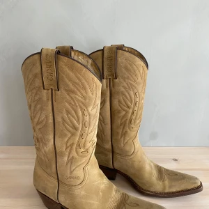 Beiga cowboy boots från Sancho - Nu säljer jag dessa as snygga cowboy bootsen/stövlarna från Sancho i storlek 39 i äkta skinn. De är i  färgen Begi mocka och har fina broderade detaljer framtill. Nypris ca 2000 jag säljer för 1500, jag kan diskutera pris vid snabb affär. De är helt nya, bara testade en gång. Säljer på grund av att de inte passade mig! Tveka inte på att höra av er om ni vill ha fler bilder eller har mer frågor!! 