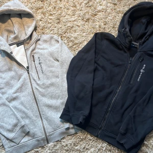 Två sailracing hoodies  - En grå och en svart sail racing hoodies, billigare vid köp av båda! Den gråa är i mycket bra skick, den svarta är i mycket bra skick men har en liten fläck i mitten men den går nog bort om man använder något speciellt medel! Skriv vid minsta fråga och ge prisförslag!🙋‍♂️