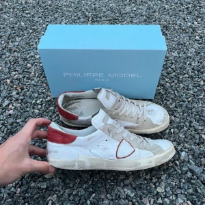 Philippe Model (prisförlAg) - Snygga vita Philippe Model sneakers med röd mockadetalj på hälen och beige partier i skinn och mocka. Lite slitna som ni kan se på bilderna men fortfarande mycket kvar att ge skorna och boxen följs med vid köp. 47.