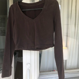Brun  Magtröja tröja - Mörkbrun croppad tröja med v-ringning och långa ärmar. Lite tjockare material så lite varmt på sommaren men annars är det väldigt mjukt o bekvämt tyg. Vid armarna är den S men magen M skulle jag säga. Ganska använd men syns inte fortfarande väldigt fin.