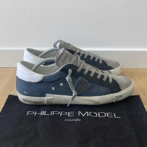 Philippe Model blå sneakers i mocka - Snygga sneakers från Philippe Model i blå mocka med grå detaljer och vit häl. Skorna har klassisk snörning, rund tå och vit sula med slitna detaljer för en cool look. Perfekta för dig som gillar streetstyle och vill sticka ut med exklusiva sneakers.