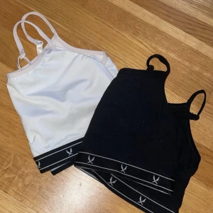 2-pack linnetoppar från Stadium - Två stilrena linnetoppar från Stadium i svart och vitt. Båda har smala axelband och elastiskt band nertill med logga och ränder. Perfekta för en sportig look eller som basplagg. Står endast storlek i den svarta, M. Men skulle säga att båda är mindre än så, den vita är något större och i ett glansigt material, medan den svarta är lite mindre och i bomull. 🤍