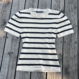 Randig topp från Gina Tricot XS - Snygg ribbad topp från Gina Tricot i storlek XS. Vit med svarta horisontella ränder, kortärmad och med rund halsringning. Perfekt för dig som gillar en klassisk men trendig stil. Materialet är mjukt och stretchigt för en bekväm passform.