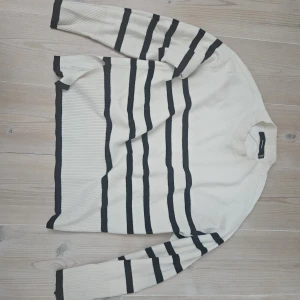 Randig stickad tröja från Vero Moda - Snygg stickad tröja från Vero Moda i krämvitt med svarta ränder. Tröjan har rund halsringning, långa ärmar och ribbade muddar. Perfekt för dig som gillar en klassisk men chill look. Passar till jeans eller kjol för en enkel stil.