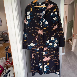 Kostym 2-delat - Blommig kavaj o byxor , svart botten m blommönster . Byxorna har resår i midjan. Svalt o skönt set . Storlek L , köpt på MQ . 